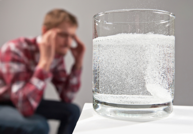 Stressed man sitting with head ache migraine near glass of water, isolated